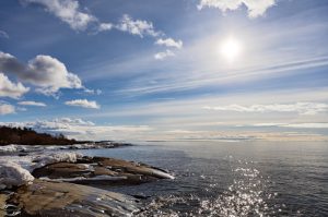 View over the sea towards the sun with the stony coast on the left
