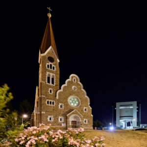 Chruch in the foreground with a modern building in the background at night