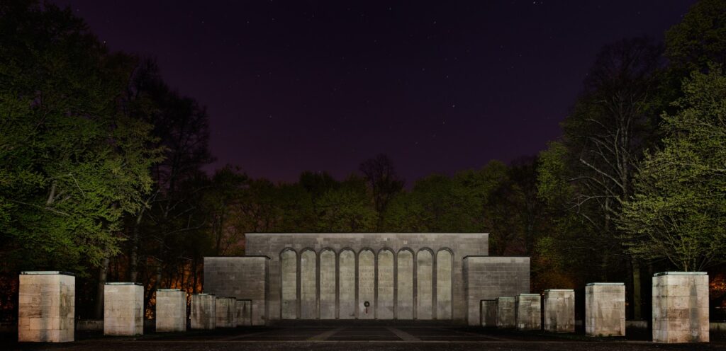 Nachtaufnahme eines monumentalen Steinmonuments mit bogenförmigen Nischen, von Bäumen umgeben.