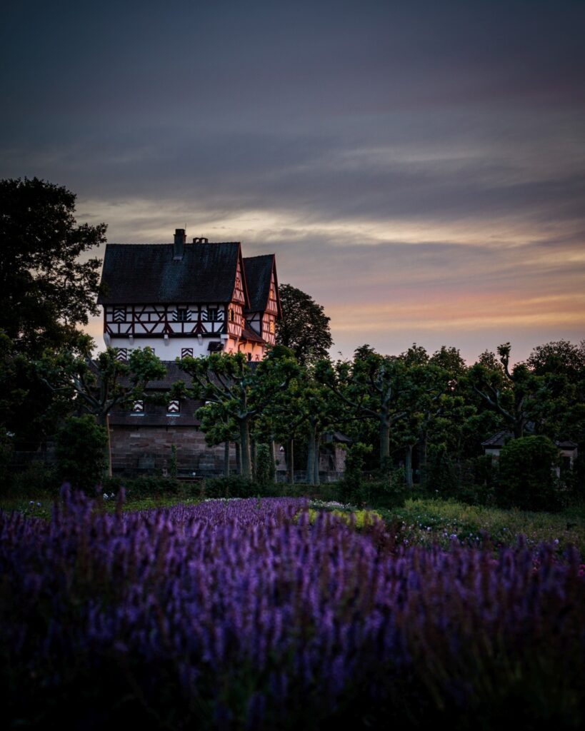 Fachwerkhaus vor einem farbenprächtigen Sonnenuntergang, umgeben von Bäumen und Grünanlagen.