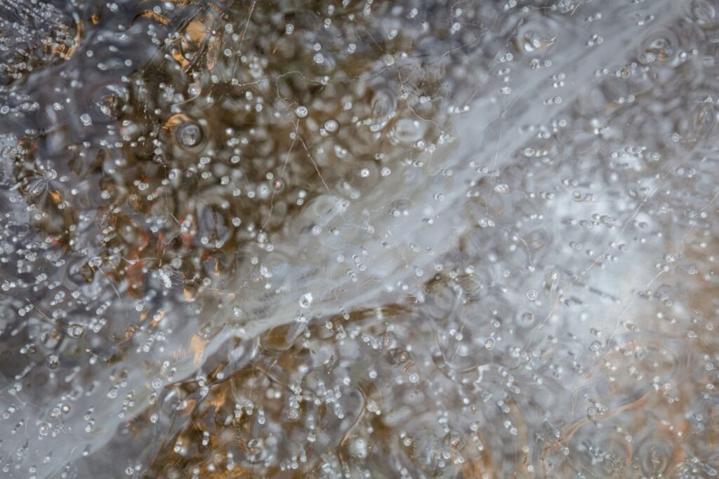 Nahaufnahme von im Eis eingeschlossenen Wassertropfen, die ein faszinierendes Muster aus Blasen und reflektierenden Lichtpunkten bilden.