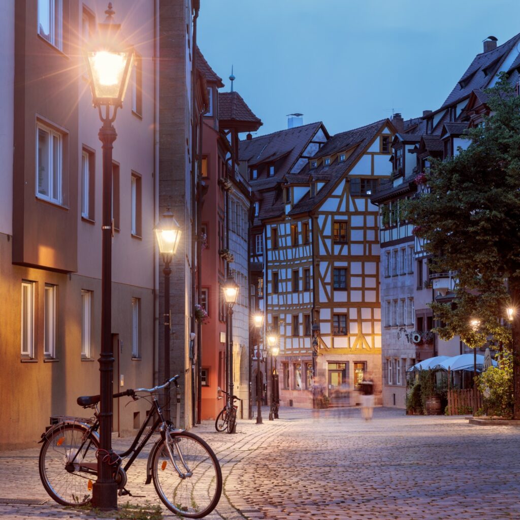 Abendliche Altstadtstraße mit Fachwerkhäusern, gepflastert und von Laternen beleuchtet; Fahrrad im Vordergrund.