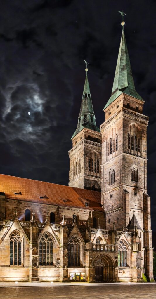 Gotische Kathedrale bei Nacht mit zwei Türmen, beleuchtete Fassade, Mond am dunklen Himmel.