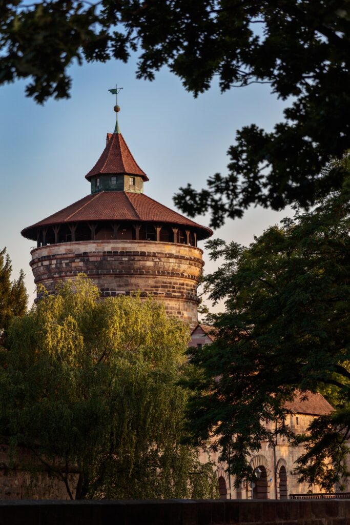 Historischer Steinrundturm mit rotem Ziegeldach, Festungsanlage, von Bäumen umgeben.