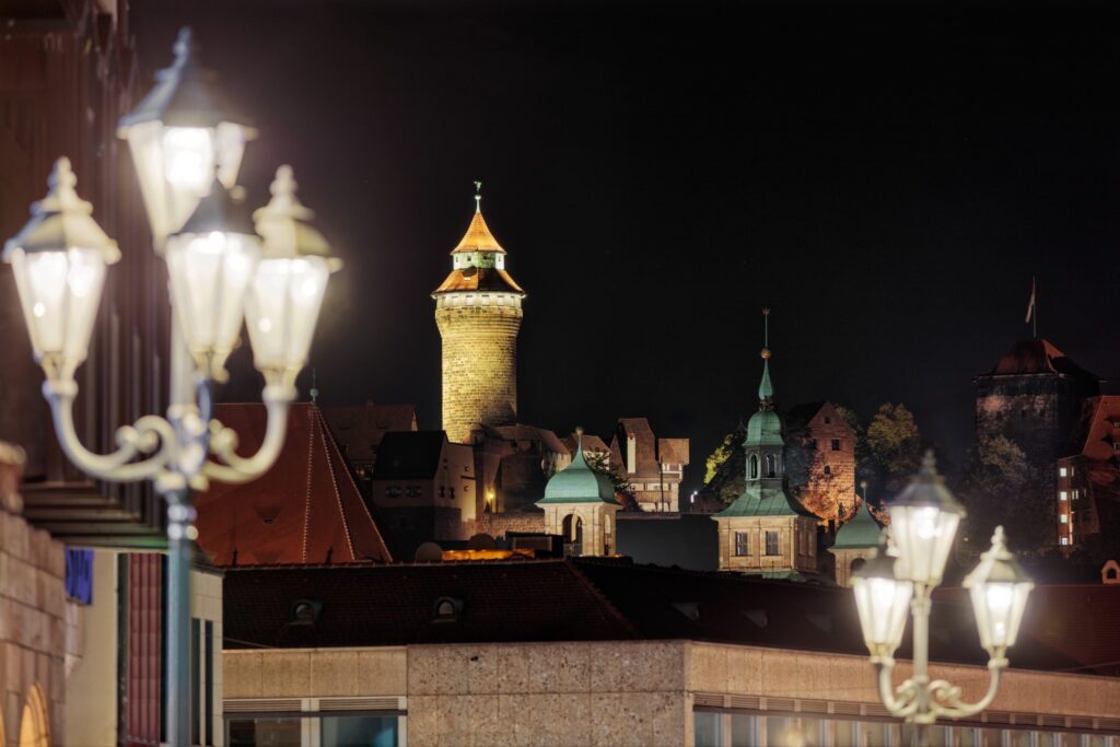 Nachtaufnahme einer historischen Stadtkulisse mit Turm, Dachlandschaft und leuchtenden Straßenlaternen