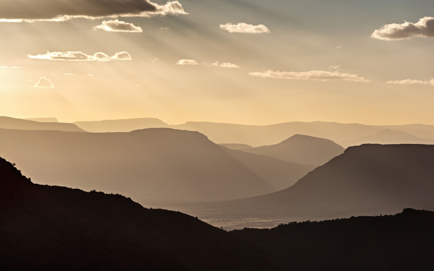 Abendstimmung über mehrstufigen Bergketten in der Wüstenlandschaft, Sonnenstrahlen durch Wolken