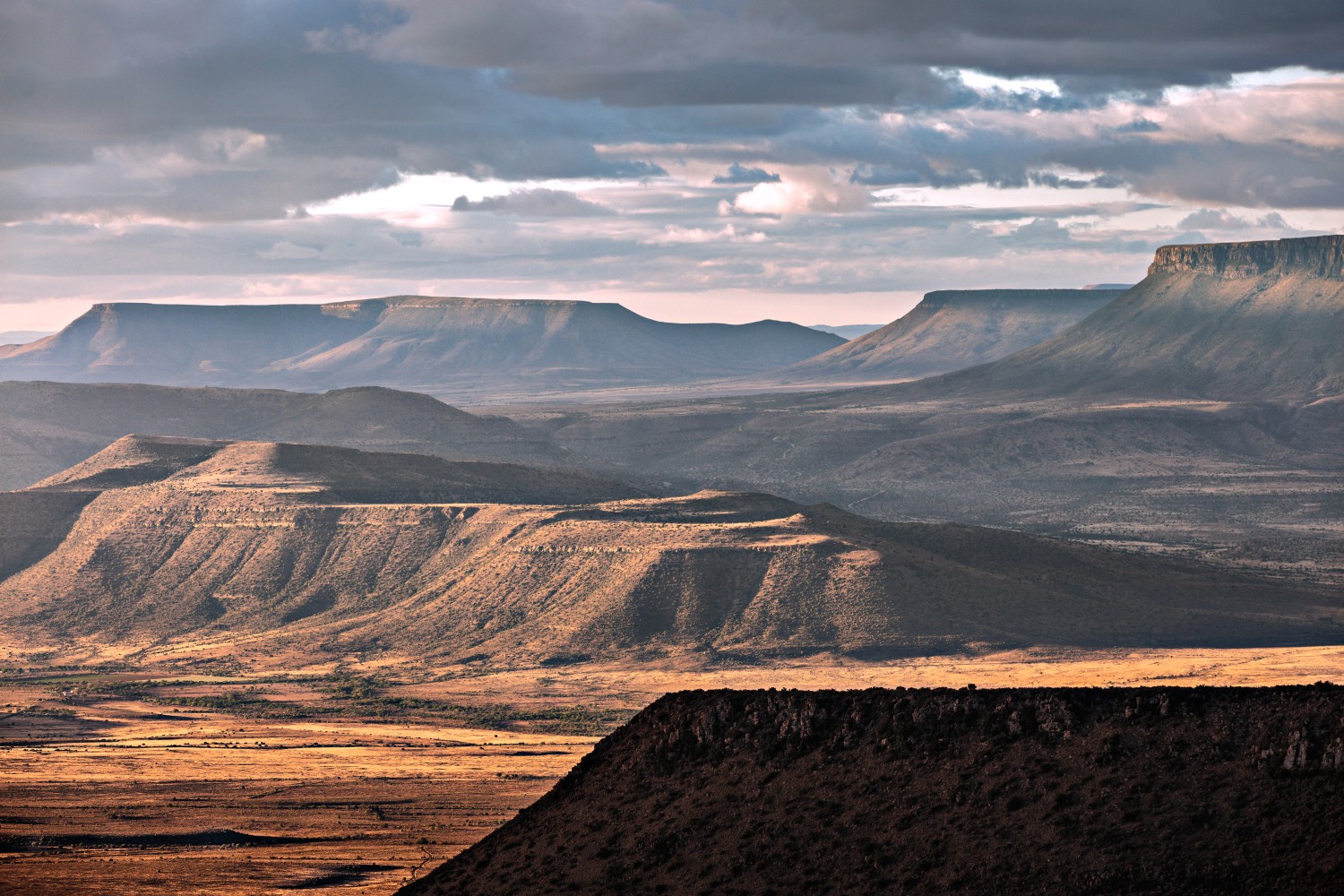 Wüstenlandschaft mit Plateaus und Mesas, sanfte Hügelzüge im warmen Abendlicht.