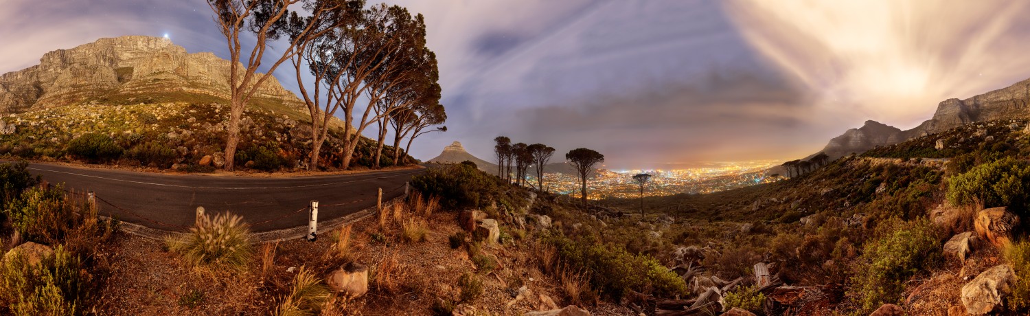 Cape Town Panorama bei Nacht: kurvige Bergstraße, Tafelberg-Umgebung, Stadtlichter am Horizont.