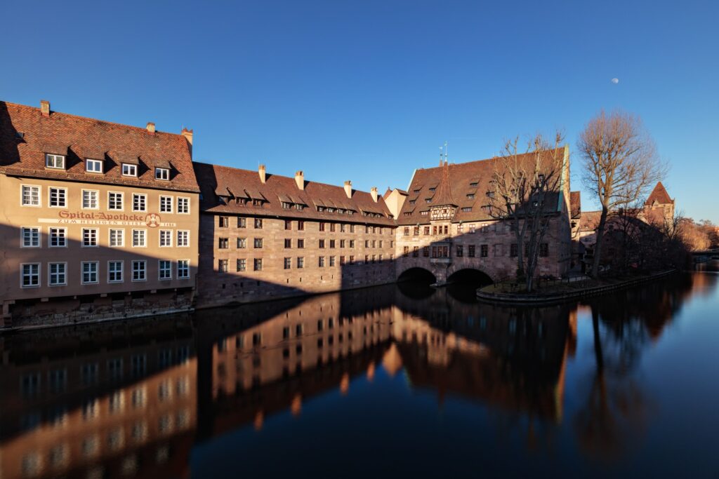 Historische Häuserfront am Fluss mit Steinbrücke, Spiegelung im Wasser; Spital-Apotheke Zum Heiligen Geist sichtbar.