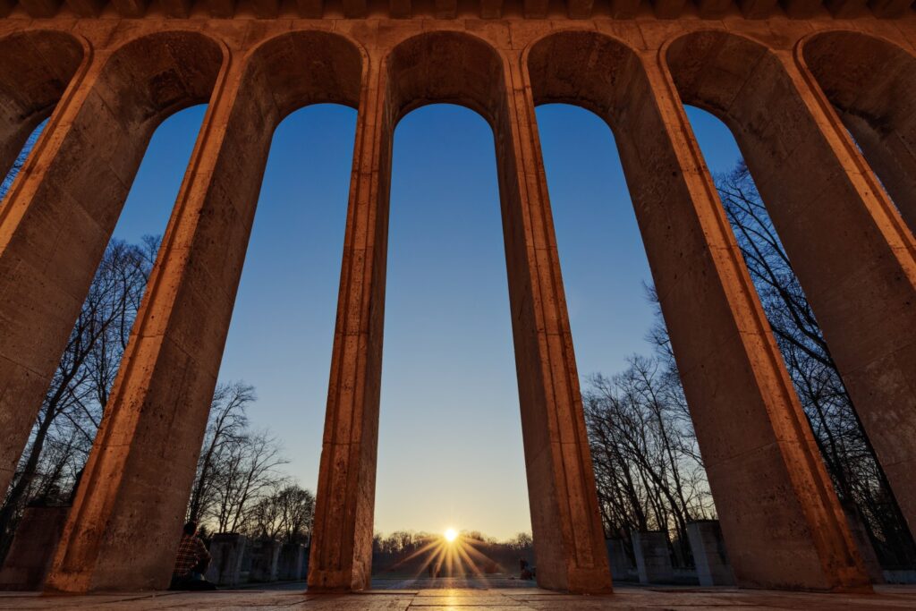 Steinerner Bogenviadukt bei Sonnenaufgang, Arkaden im Vordergrund, winterliche Bäume im Hintergrund, warme Lichtstimmung.