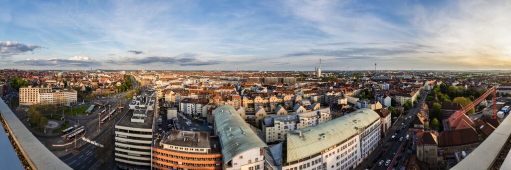 Panorama einer deutschen Großstadt von oben: Dächer, Straßen und moderne Gebäude vor blauem Himmel.