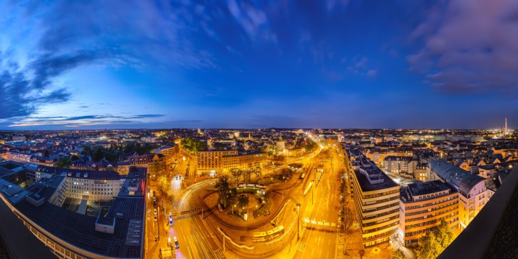 Nachtpanorama einer europäischen Großstadt mit beleuchteten Straßen, Kreisverkehr und Rundplatz, Skyline.