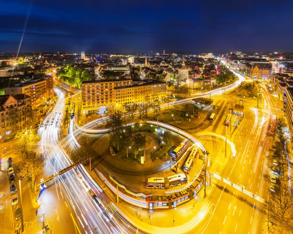 Nachtaufnahme einer hell erleuchteten Stadt mit Kreisel, langen Lichtspuren und urbaner Skyline