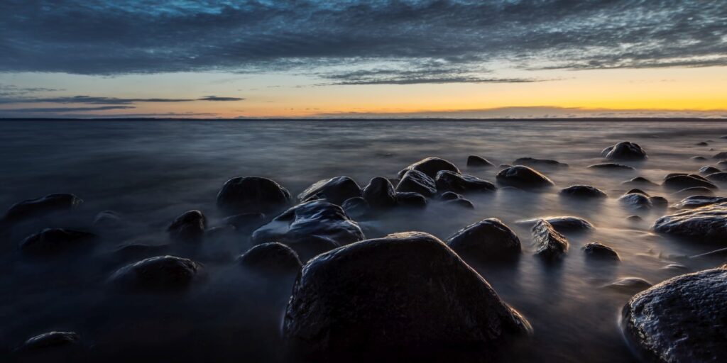 Ruhiger Küstenabschnitt mit großen glatten Steinen im Meerwasser bei Sonnenuntergang.