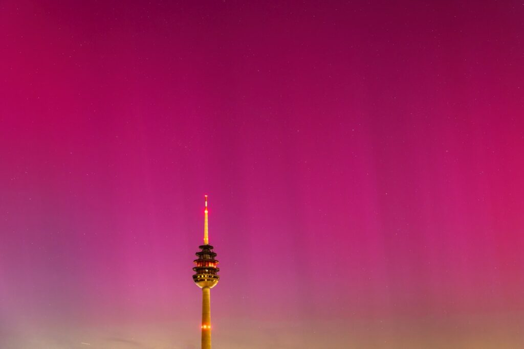 Ein schlanker Turm mit leuchtenden Lichtern ragt unter einem intensiven magentafarbenen Himmel empor, der mit unzähligen Sternen übersät ist und zum Horizont hin heller wird.