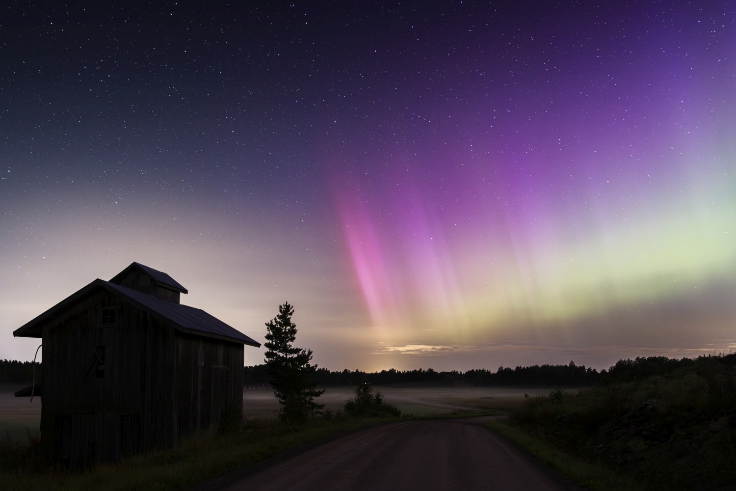 Nordlichter (Aurora borealis) über einer einsamen Holzhütte, Sternenhimmel und nebliger Landstraße bei Nacht.