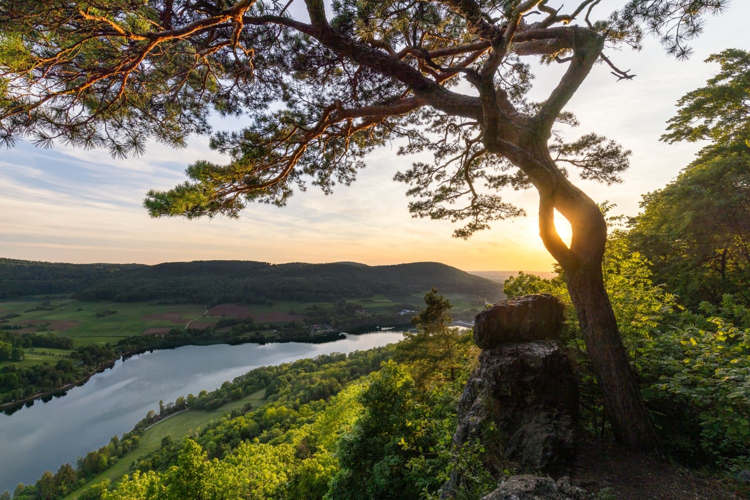 Sonnenuntergang über einer Flusslandschaft; Blick von einem Felsvorsprung auf grüne Täler und einen ruhigen Fluss.