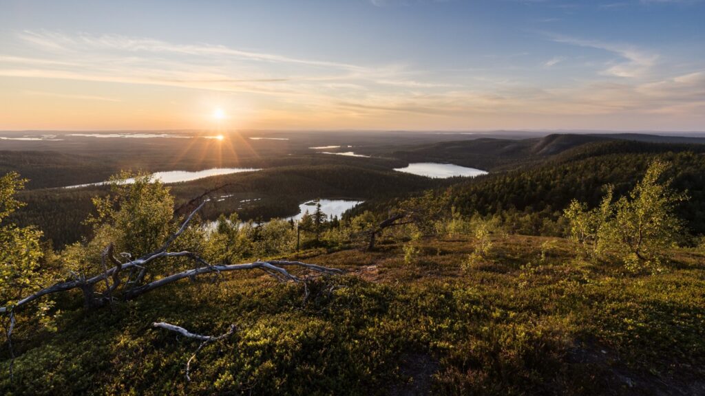 Panoramablick auf eine malerische Landschaft mit Wäldern und Seen bei Sonnenuntergang, der die Natur in warmen Farben erleuchtet.