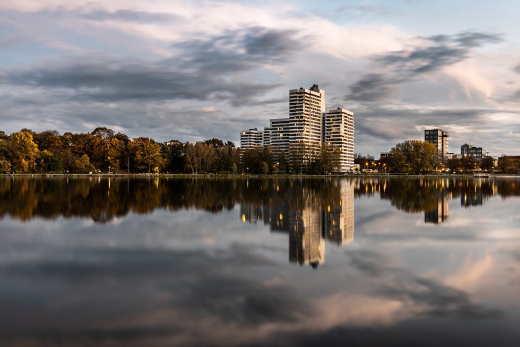 Moderne Hochhäuser am Seeufer mit Herbstlaub; ruhige Wasserreflexion der Skyline bei Dämmerung.