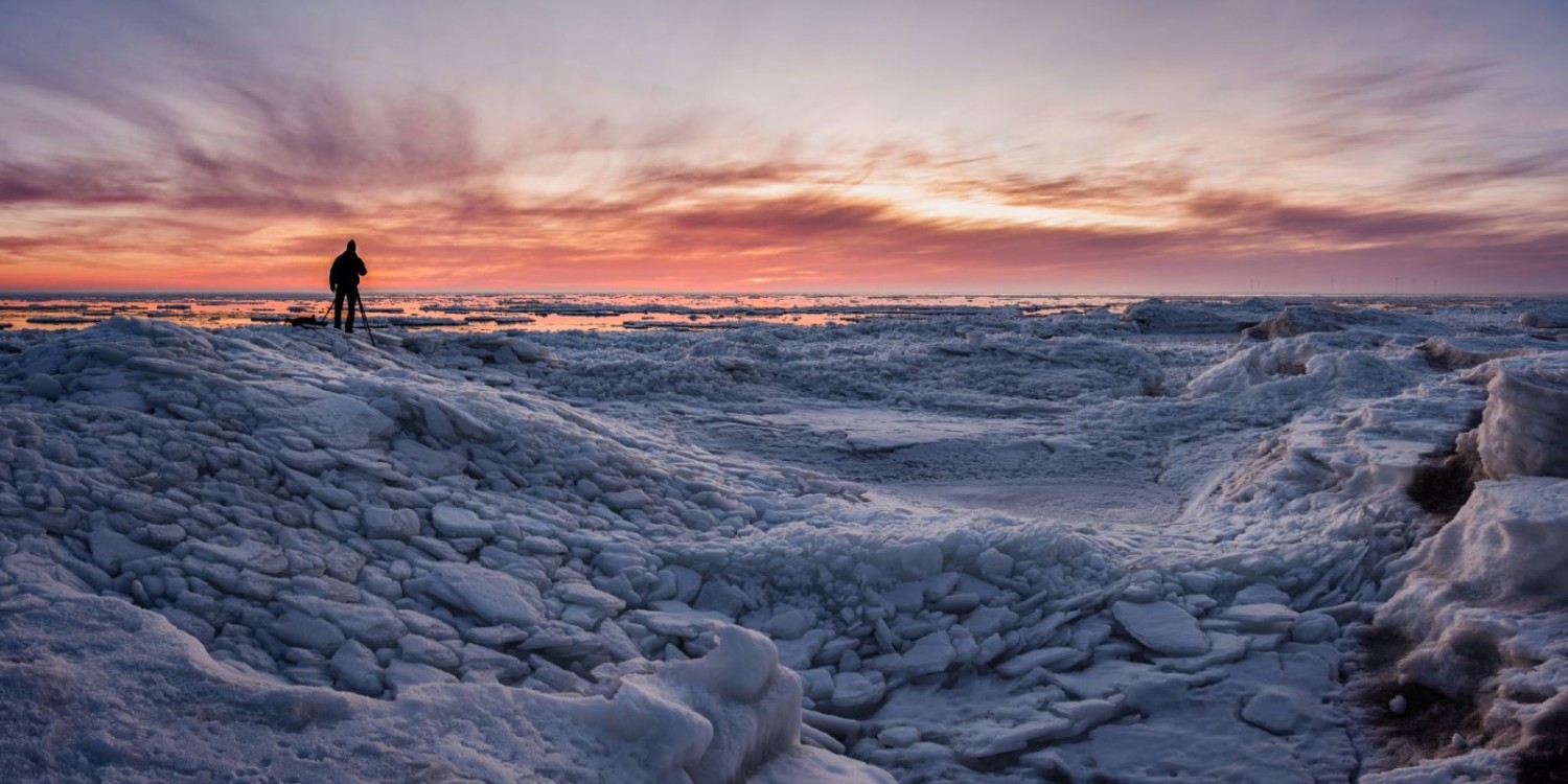 Fotograf auf brüchigem Eisfeld bei Sonnenuntergang; eindrucksvolle Eislandschaft und farbiger Himmel