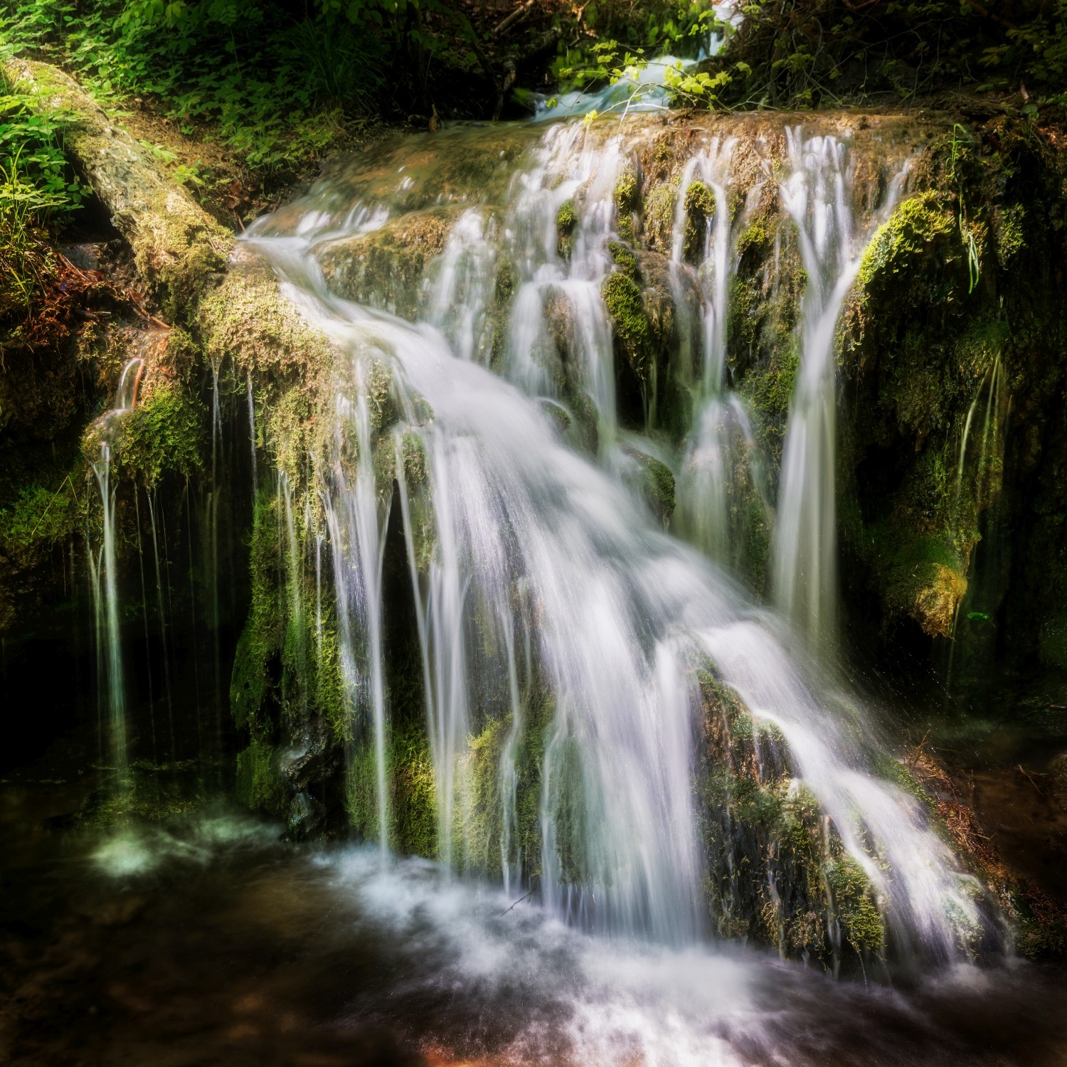 Wasserfall im Wald mit moosigen Felsstufen und sanften Kaskaden, grüne Naturkulisse.