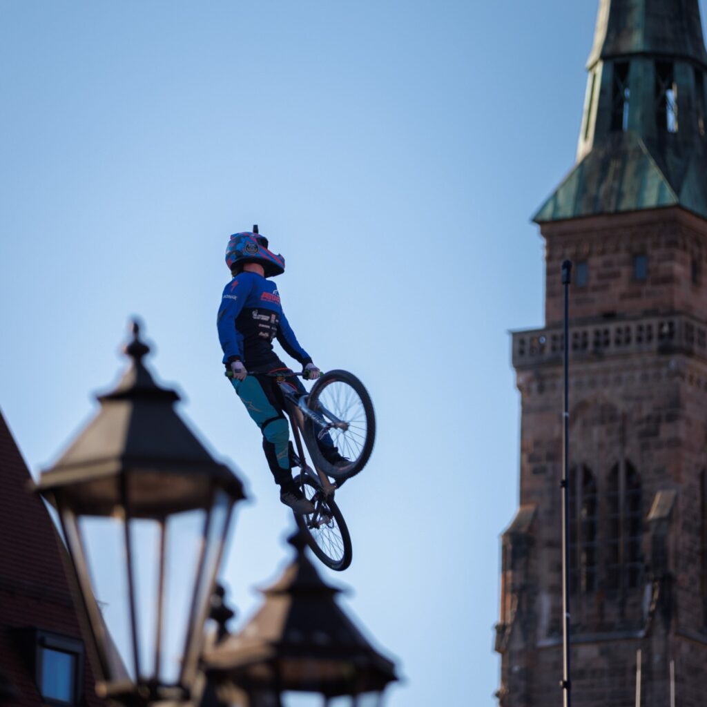 Fahrrad-Trick in der Luft vor historischer Stadtkulisse mit Kirchturm und Straßenlaternen