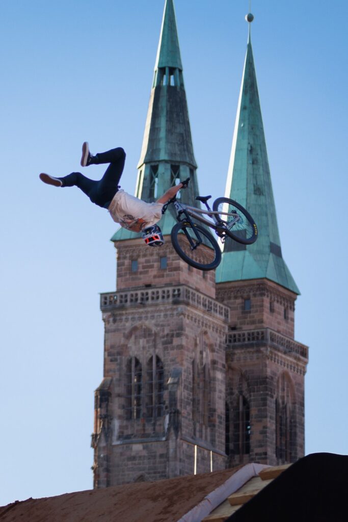 BMX-Stuntfahrer führt Backflip neben gotischen Kirchtürmen aus – Freestyle-Bike-Sprung über Stadtzentrum