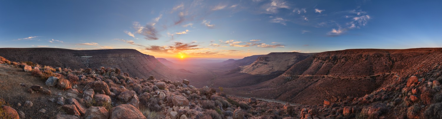 Panorama einer Wüstenlandschaft mit Felsbrocken und Canyon im Sonnenuntergang, warmes Abendlicht über dem Tal.
