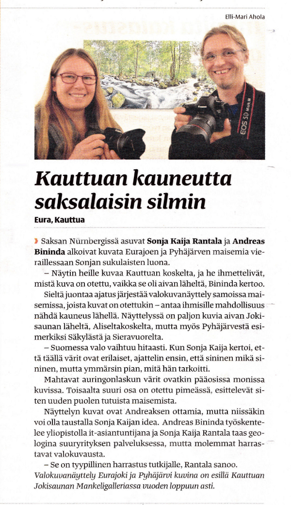 Zwei Fotografen mit DSLR-Kameras posieren vor einem Landschaftsbild, abgedruckt in einem Zeitungsartikel.