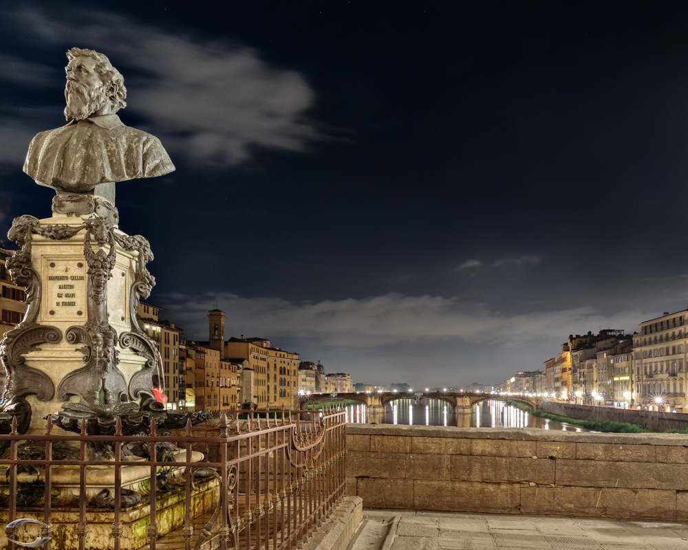 Nachtaufnahme einer Statue auf einem Brunnensockel am Arno in Florenz, beleuchtete Uferpromenade und Spiegelungen der Brückenlichter im Wasser