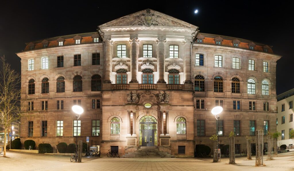Nachtaufnahme eines historischen Gebäudes mit Säulenportal, Bogenfenstern und Treppenstufen, warm beleuchtet auf dem Stadtplatz.