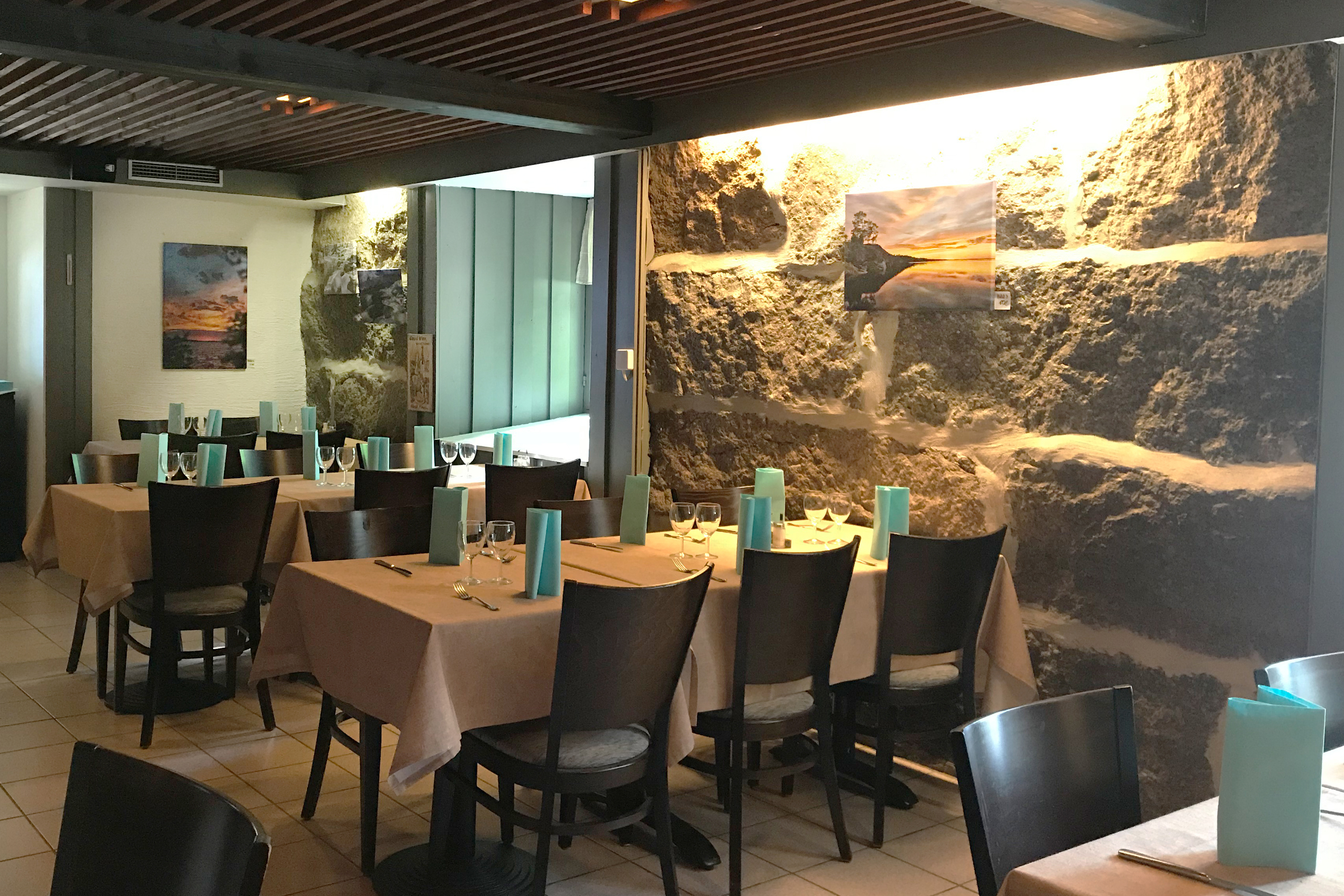 Gemütliches Restaurant mit Steinwand, gedeckten Tischen, dunklen Stühlen und türkisfarbenen Servietten.