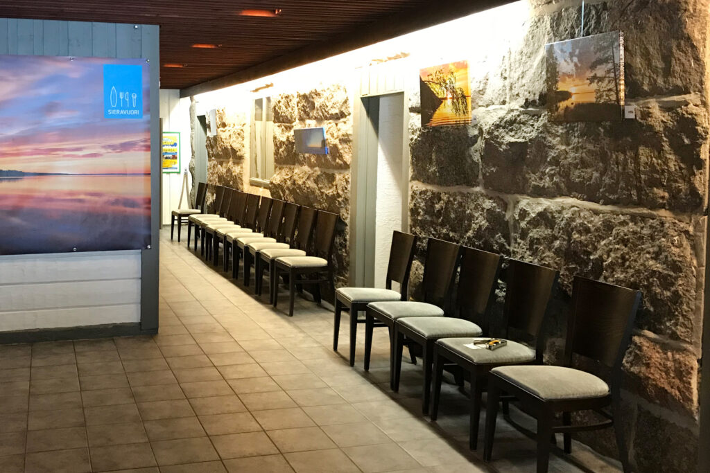 Warteraum mit Steinwand, lange Stuhlreihen gepolsterter Sitze, Wandfotos und ruhiges Licht.