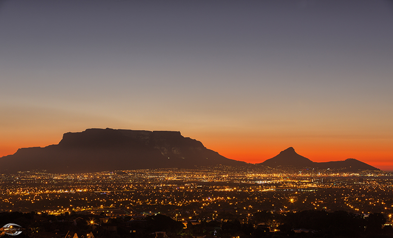 Sonnenuntergang über Cape Town mit Tafelberg und Lion's Head, beleuchtete Stadtlichter unten.