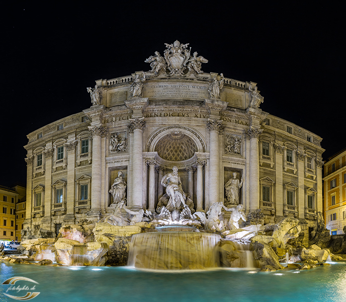 Nachtaufnahme des Trevi-Brunnens in Rom: beleuchtete Barockfassade, Skulpturen und glitzerndes Wasser.
