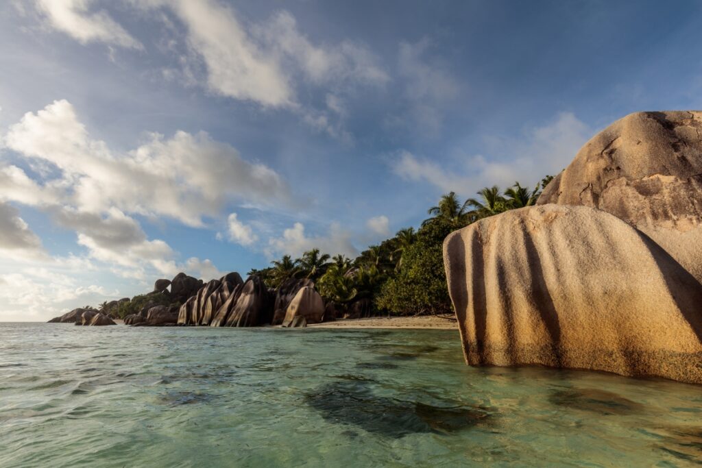 Tropischer Strand mit großen Granitfelsen, Palmen, klarem türkisblauem Wasser und sanften Wellen
