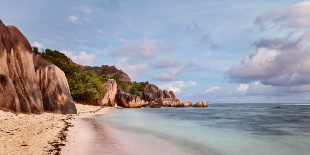 Tropische Strandlandschaft mit großen Granitfelsen, hellem Sand, klarem Wasser und blauem Himmel.