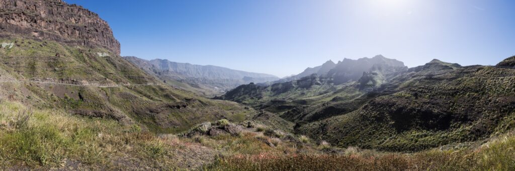 Panorama einer canyonartigen Berglandschaft mit grüner Vegetation, felsigen Schluchten und klarem blauen Himmel.