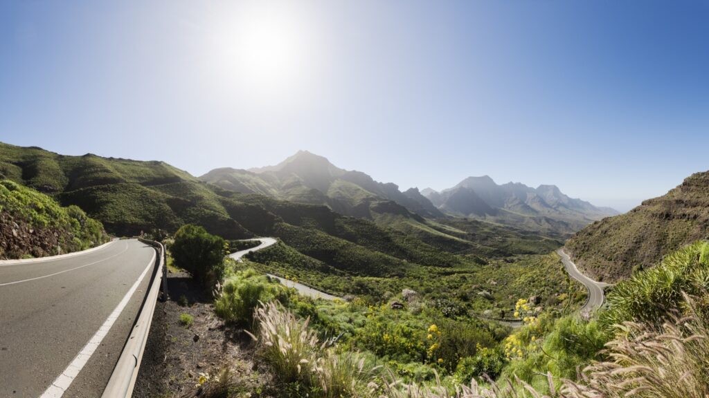 Kurvenreiche Serpentinenstraße durch grüne Berglandschaft unter strahlend blauem Himmel – sonniger Ausblick.
