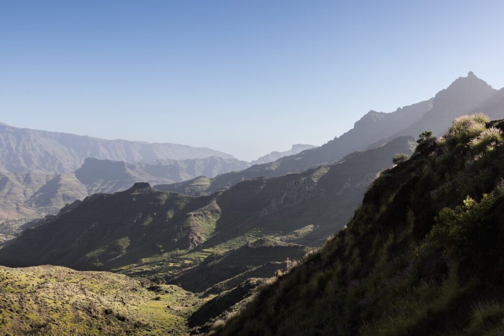 Atemberaubende Berglandschaft mit grünen Hängen, tiefen Tälern und schroffen Gipfeln unter klarem Blau.