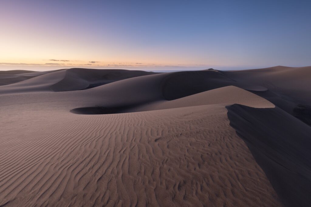 Wüstenlandschaft mit sanften Sanddünen und windgeformten Kämmen bei Sonnenuntergang, Farbenverlauf des Himmels