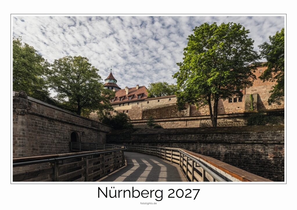 Historische Nürnberger Stadtmauer mit Turm, Holzweg am Burggraben, von Bäumen gesäumt, wolkiger Himmel